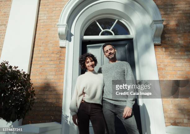 portrait happy couple standing at front door on sunny house stoop - 40s couple sunny stockfoto's en -beelden