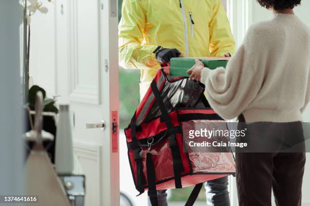 woman receiving pizza delivery from delivery man at front door - take away food courier stock pictures, royalty-free photos & images