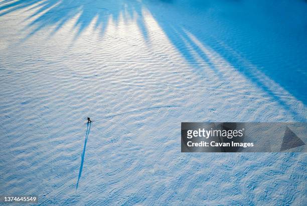 tiny figure and shadow of lone skier on frozen lake, maine - long shadow stock pictures, royalty-free photos & images