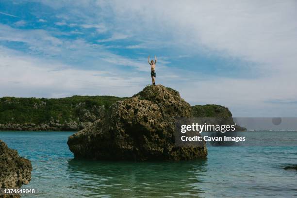 boy on top of ocean rock formation in blue sky summer - okinawa blue sky beach landscape stockfoto's en -beelden
