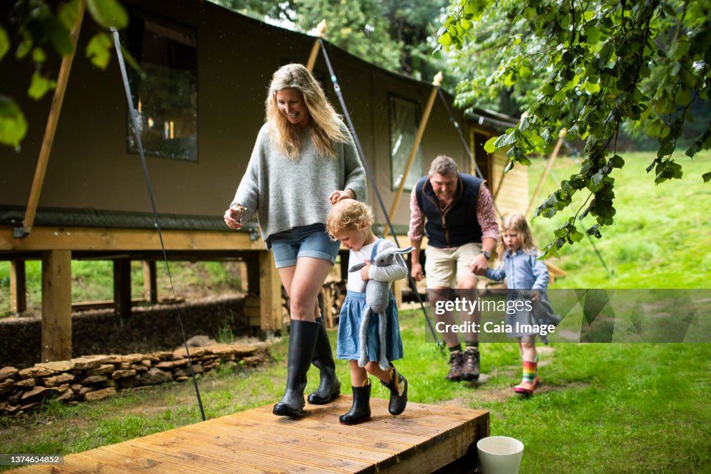 Happy family holding hands walking outside cabin in woods