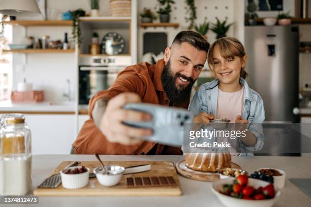 father and daughter taking a selfie while decorating a cake in the kitchen - beard trimming stock pictures, royalty-free photos & images