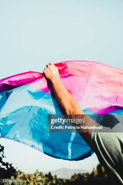 young latino man holding the bisexual pride flag in a rural spot. lgtbiq+ and sexual diversity concept. - bi annual stock-fotos und bilder