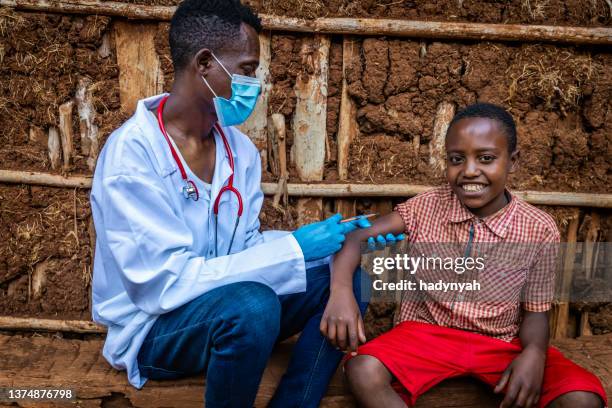 doctor is doing an injection to young african boy in small village, east africa - vaccine africa stock pictures, royalty-free photos & images