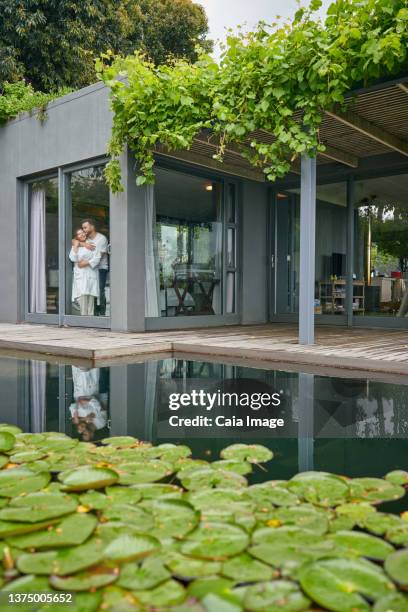 affectionate couple at window of modern house - pont architecture stock pictures, royalty-free photos & images