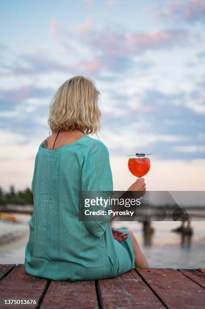 rear view of a woman holds a glass of red cocktail on a wooden pier during sunset - hands behind glass stock pictures, royalty-free photos & images