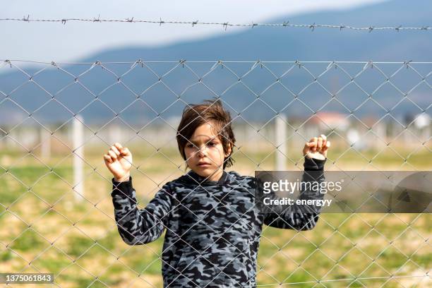 petit garçon derrière la clôture - fil barbelé photos et images de collection