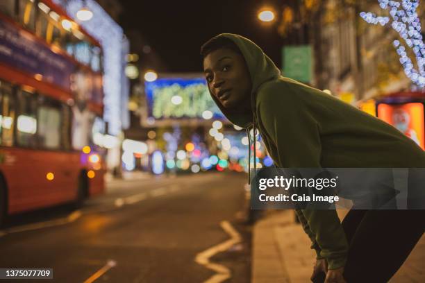 young female jogger waiting to cross city street at night, london, uk - standing with hands on knees imagens e fotografias de stock