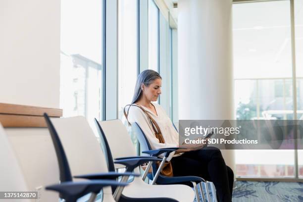 woman uses smart phone while sitting in waiting room - geduld stockfoto's en -beelden