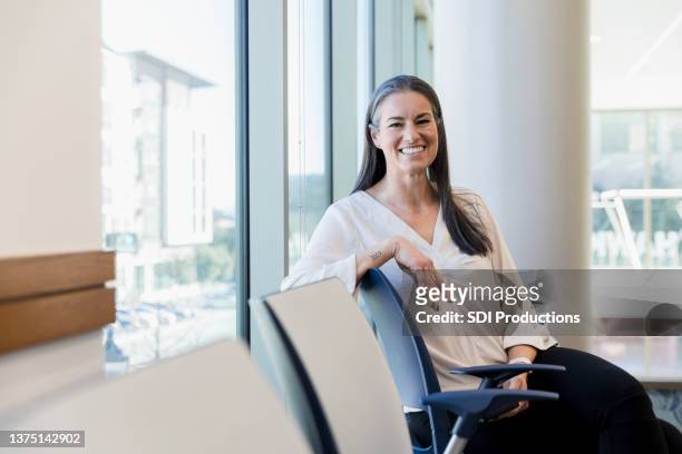 mittelgroße frau, die im wartezimmer sitzt, lächelt für die kamera - patientin stock-fotos und bilder