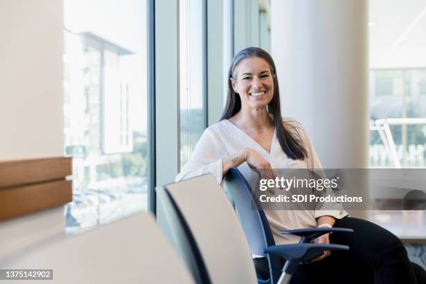 mid adult woman sitting in waiting room smiles for camera - blank room stockfoto's en -beelden