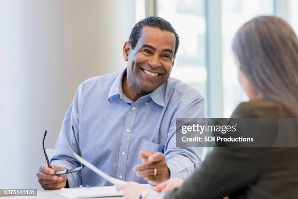 reifer arzt lächelt, während er dokumente mit weiblicher administratorin bespricht - african american business man stock-fotos und bilder