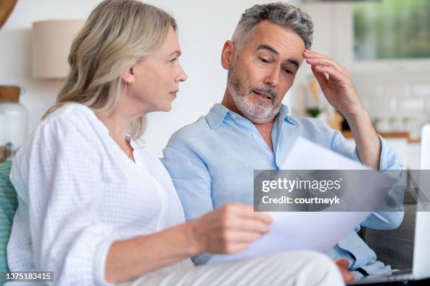 pareja madura haciendo papeleo con una computadora portátil en casa. - shock fotografías e imágenes de stock