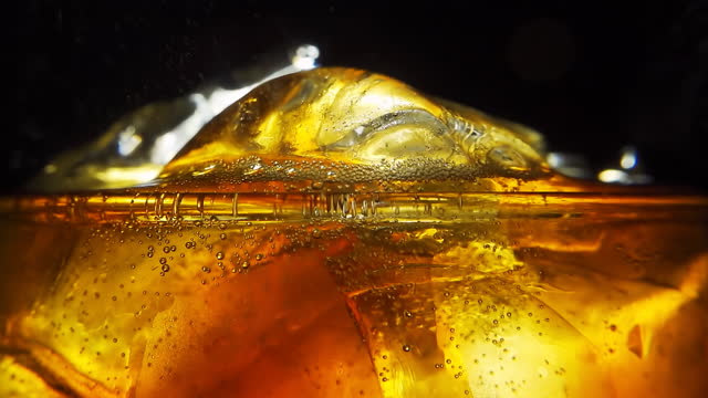 Soda is pouring into a glass with ice cubes isolated on a black background. Overflowing wet glass with pop soda. 4k macro video with speed ramp effect.