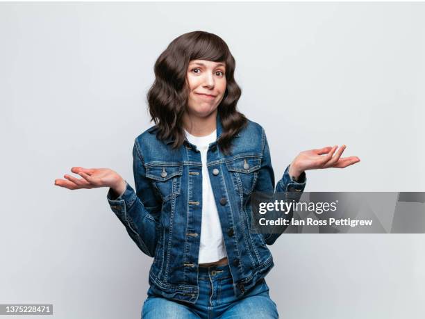 cute latina woman wearing denim jacket, making a face - shrug shoulders stock-fotos und bilder