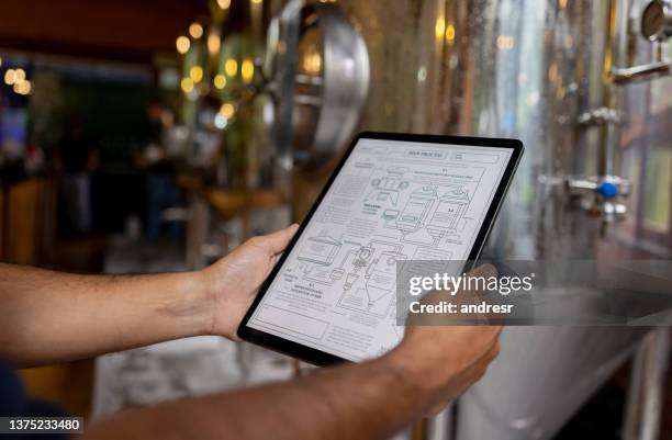 close-up on a man using a tablet computer to control the production line at a brewery - brewmaster stockfoto's en -beelden