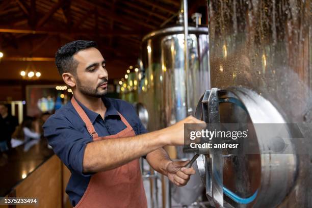 man working at a brewery and closing one of the distillery stills - microbrewery stock pictures, royalty-free photos & images