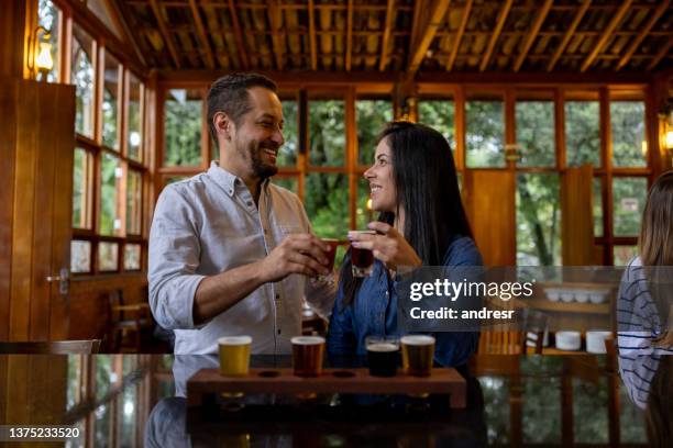 happy couple making a toast while trying different beers at a brewery - craft brewery stock pictures, royalty-free photos & images