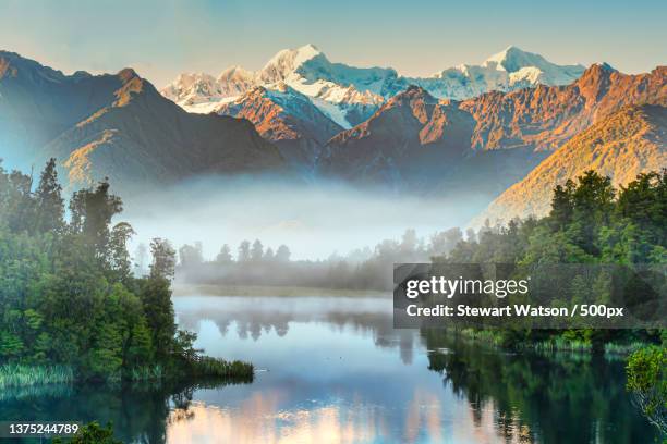 early moring fog at lake matheson,scenic view of lake by mountains against sky,lake matheson,west coast,new zealand - lake matheson new zealand stock pictures, royalty-free photos & images
