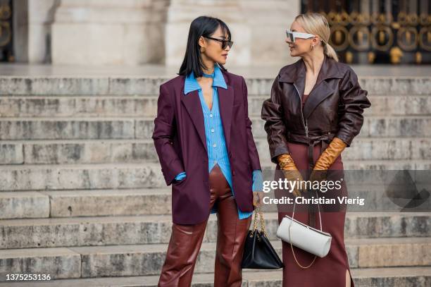 Pornwika Spiecker is seen wearing bordeaux blazer, blue button shirt, brown suede pants, heels & Justyna Czerniak wearing rust brown dress, brown...