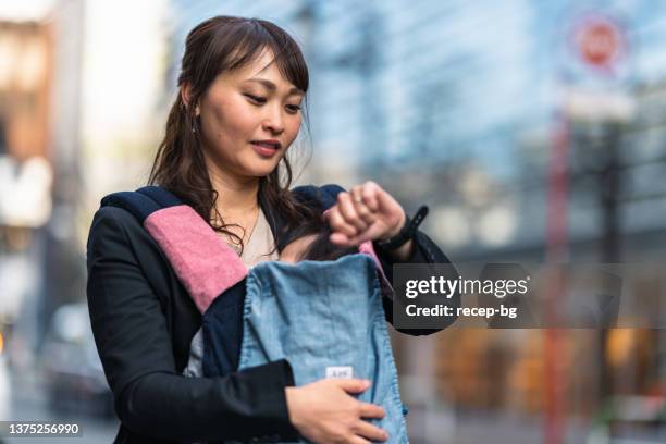 working mother commuting with her small baby while using smart watch in the city - single mother working stock pictures, royalty-free photos & images
