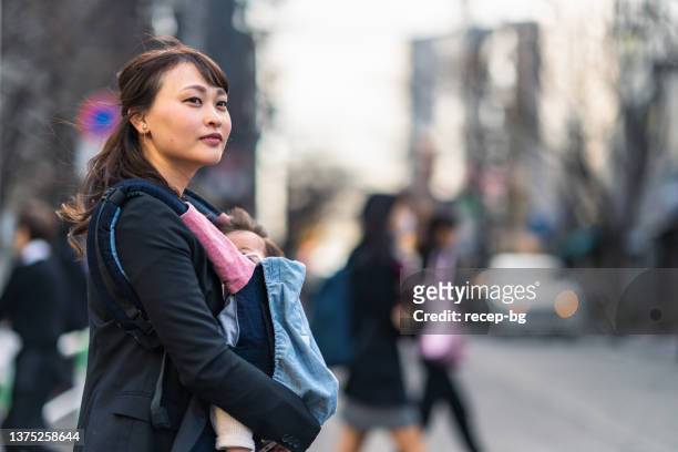 working mother commuting in the city with her baby - baby carrier stock pictures, royalty-free photos & images