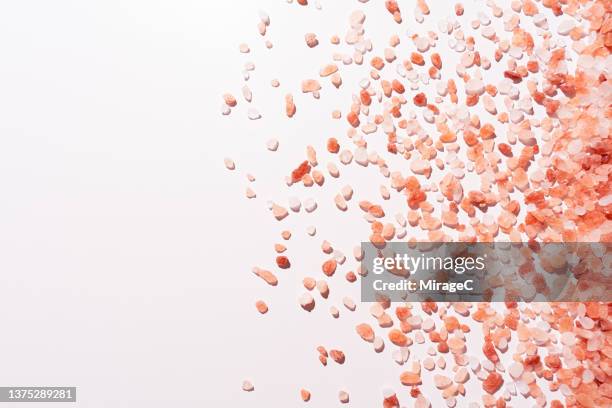 spilled himalayan pink salt grains on pink background - himalayan salt stock pictures, royalty-free photos & images