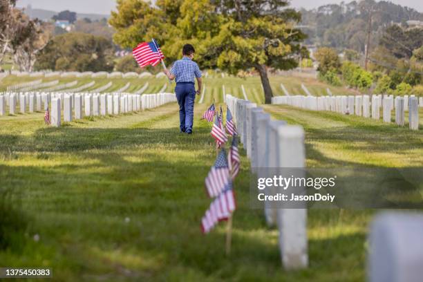 kleiner junge platziert flaggen auf veteranengrab - memorial day flag ceremony stock-fotos und bilder