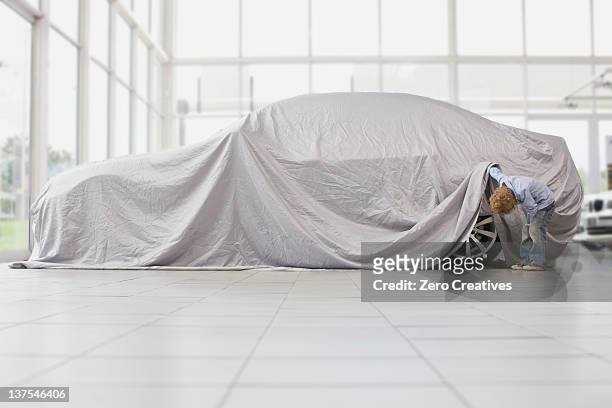 boy peeking under cloth on car - covered car photos et images de collection