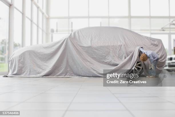 boy peeking under cloth on car - car inside showroom stock pictures, royalty-free photos & images