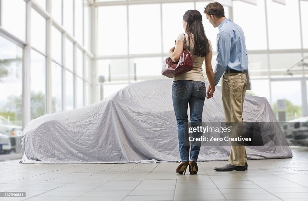 Couple admiring new car under cloth