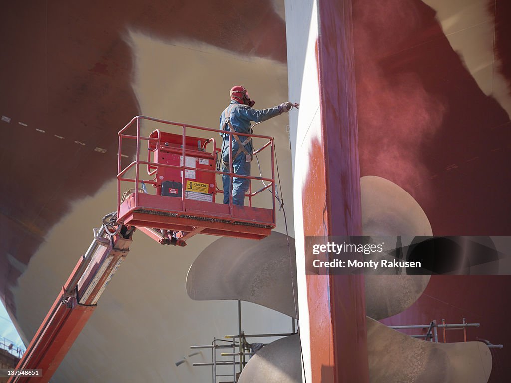 Worker spraying underside of ship in dry dock
