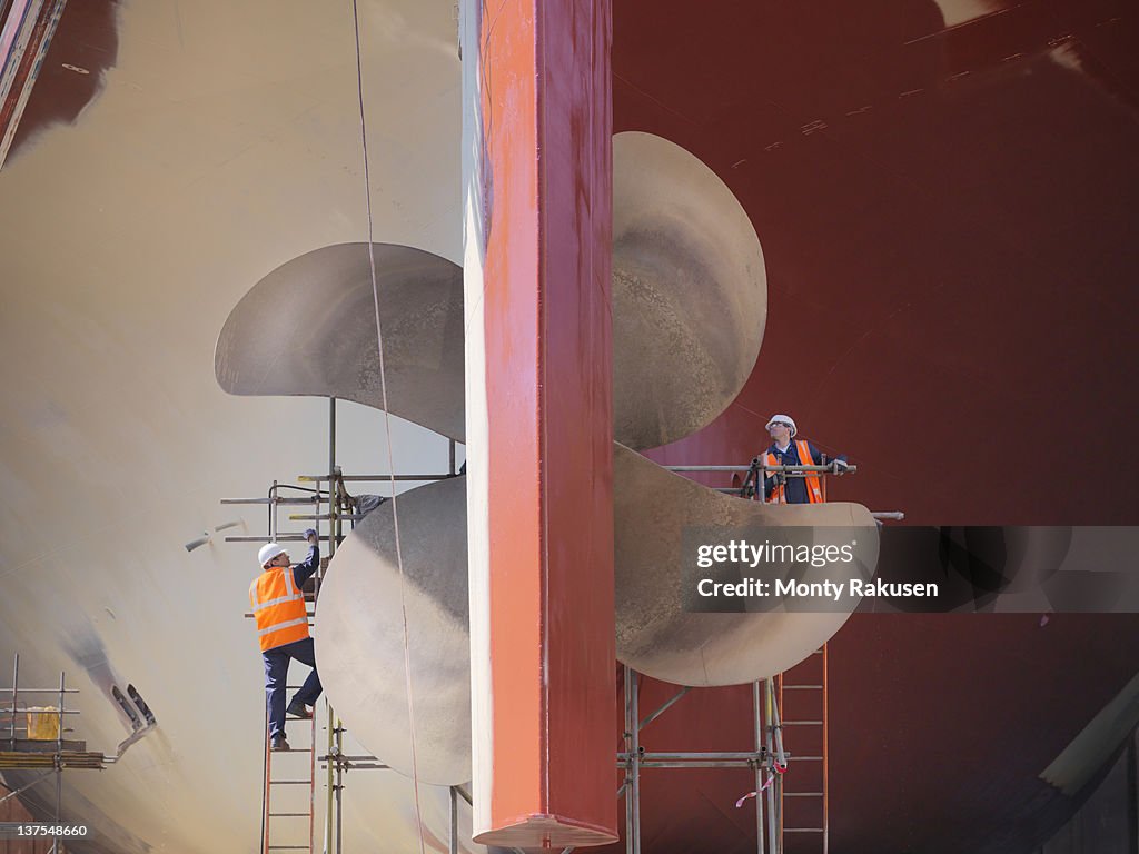 Workers checking underside of ship in dry dock