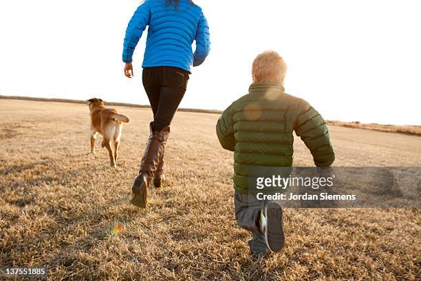 mom and young boy running with their dog. - family dog stock-fotos und bilder