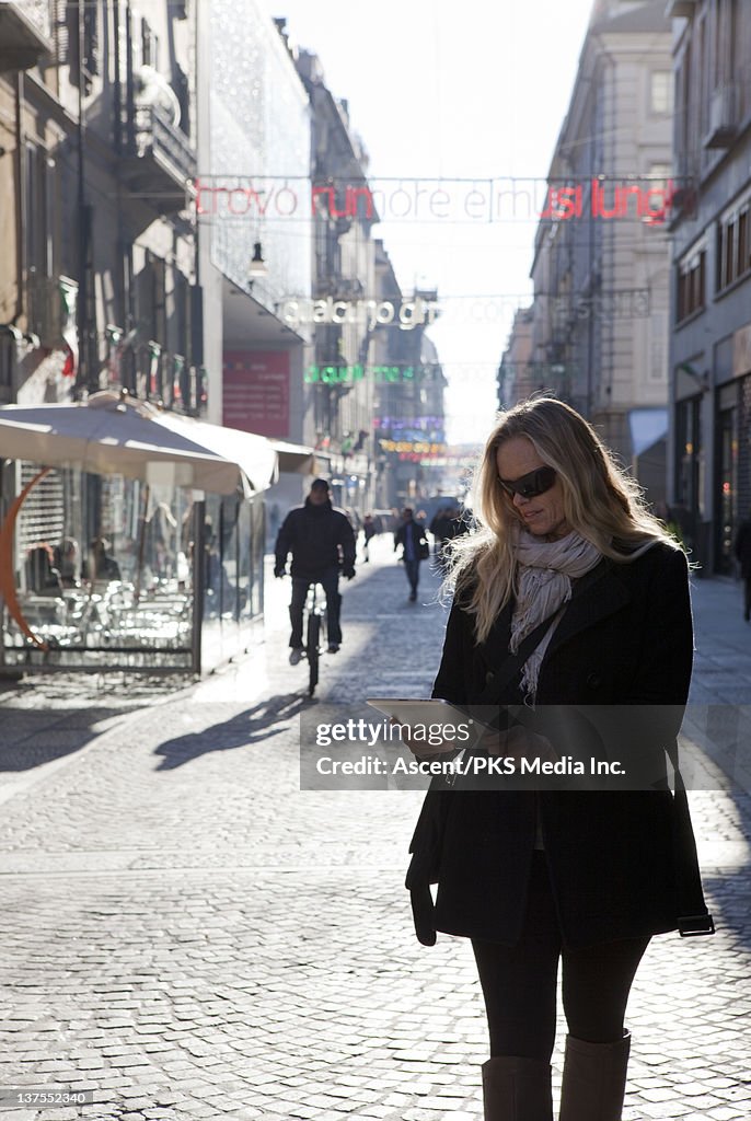 Woman consults digital tablet, walking in city