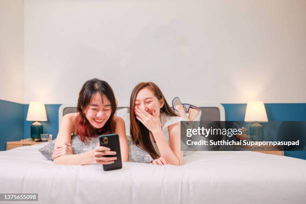 two asian females' enjoys using their smartphone and taking their photo on the bed. - asian girl doing online shopping ストックフォトと画像