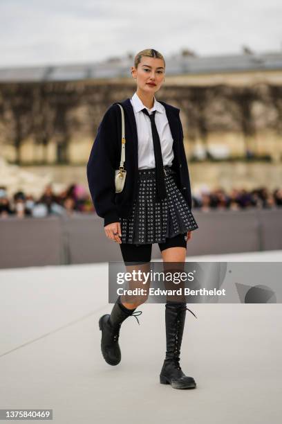 Amalie Gassmann wears silver earrings, a white shirt, a black tie, a black oversized buttoned cardigan, a beige matte leather Bobby handbag from...