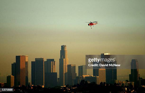 An Erickson Aircrane firefighting helicopter flies past a slightly smokey downtown Los Angeles skyline as it returns from picking water at an...