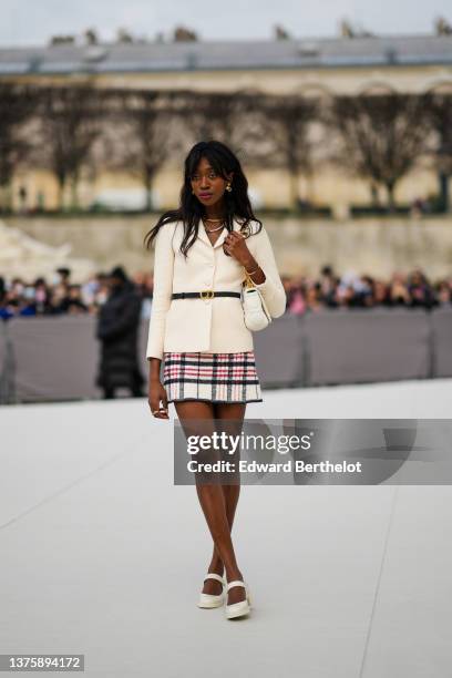 Emmanuelle Koffi wears gold and pearls pendant earrings, gold necklaces, a white pearls necklace, a white latte blazer jacket, a black shiny leather...