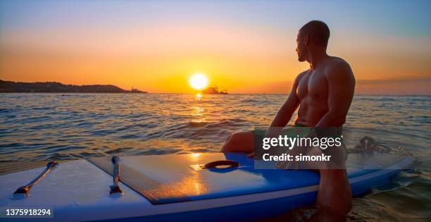 man sitting on paddle board - paddle board men imagens e fotografias de stock