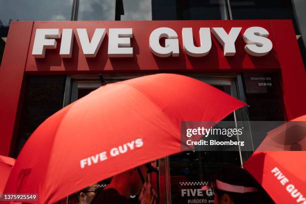 Customers hold umbrellas while waiting in line to enter the first outlet of US burger restaurant chain Five Guys in the Gangnam District of Seoul,...