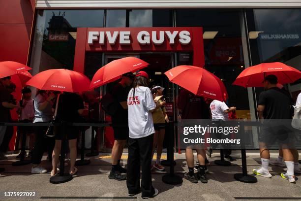 Customers hold umbrellas while waiting in line to enter the first outlet of US burger restaurant chain Five Guys in the Gangnam District of Seoul,...