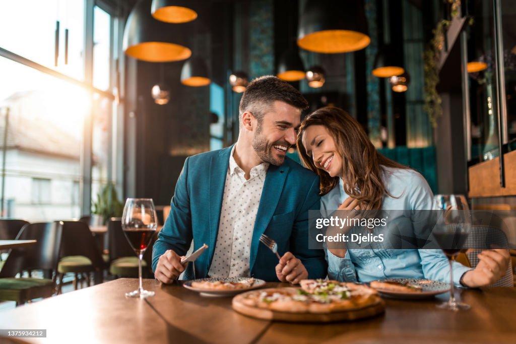 Couple enjoué mangeant une pizza ensemble dans un restaurant.
