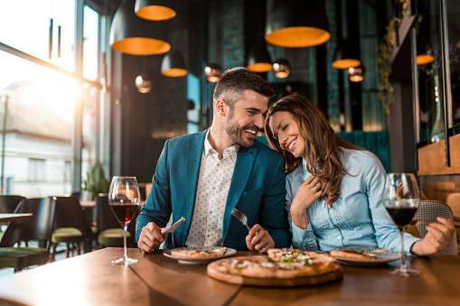 Playful couple eating pizza together in a restaurant.