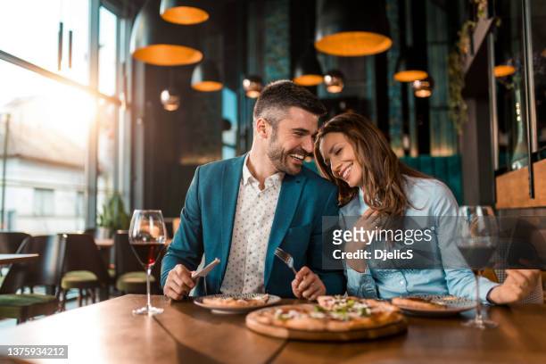 playful couple eating pizza together in a restaurant. - fancy restaurant stock pictures, royalty-free photos & images