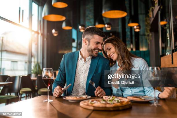 playful couple eating pizza together in a restaurant. - elegancia imagens e fotografias de stock