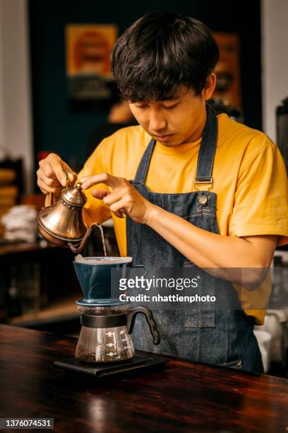 young male asian barista in yellow shirt and blue apron making brewing coffee using kalita coffee maker - vietnamese ethnicity imagens e fotografias de stock
