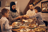 Traditional Muslim parents and their kids sharing pita bread during family dinner on Ramadan