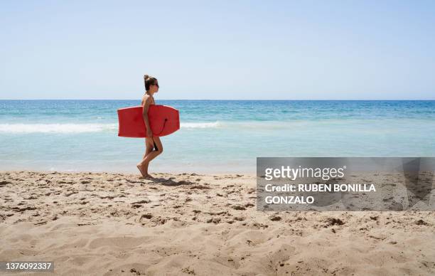 caucasian teenager carrying surfboard on beach. vacation concept. - beach girl ストックフォトと画像