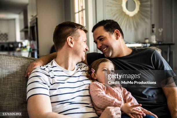 portrait of gay couple with toddler daughter in living room - persona lgbtqi foto e immagini stock